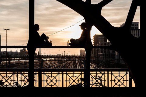 Two people sitting on the parapet and drinking against the light