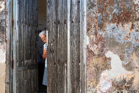 Woman at the entrance of her house with a decayed facade of crumbling plaster and a weathered wooden door