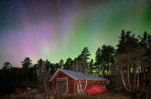 Northern lights above a wooden cabin in a Nordic forest