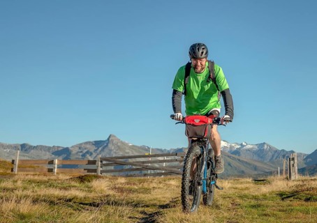 Mountain biker in his late forties rides on an ebike along an alpine path against a blue sky