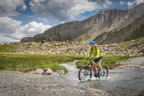 Mountain biker rides on alpine gravel road through mountain river