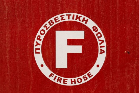 Close-up of red and white painted metal cabinet cover with Fire Hose written in Greek and English languages