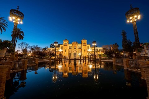 Illuminated art museum Museo de Artes y Costumbres Populares de Sevilla reflected in a fountain