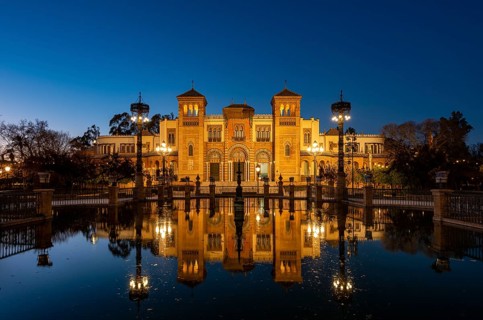 Illuminated art museum Museo de Artes y Costumbres Populares de Sevilla reflected in a fountain