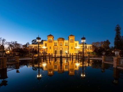 Illuminated art museum Museo de Artes y Costumbres Populares de Sevilla reflected in a fountain