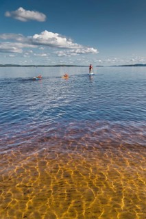 Woman on standup paddling board and children on air mattresses