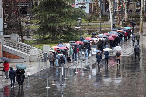 Tourists from abroad stand by the line with their umbrellas to get a ticket for a visit to the Prado Museum on a rainy sunday in Madrid