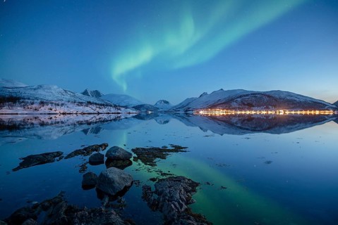 Aurora borealis above snow-capped peaks reflected in a fjord