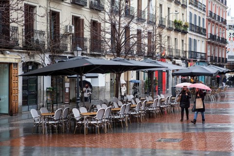 Empy seats in terraces of chueca square in the gay district as people walks by on a rainy day