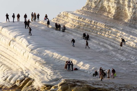 Tourists hiking on chalk cliffs Scala dei Turchi in the evening