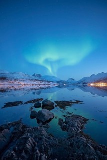 Aurora borealis above snow-covered peaks reflected in a fjord