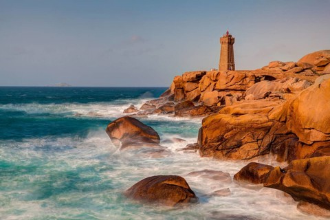 Lighthouse on red granite rocks and rough sea