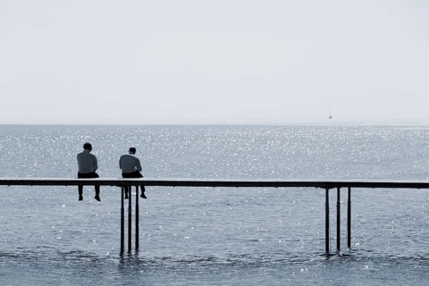 Two men sitting on a bathing jetty by the sea