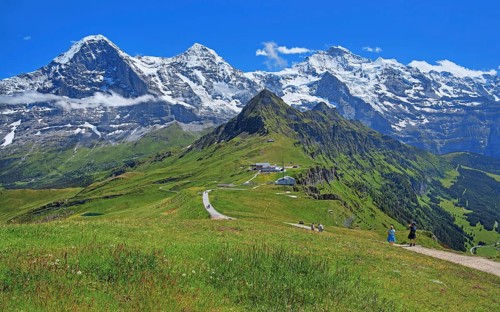 Mountain meadow and hiking trail on the Maennlichen with the triumvirate of the Eiger