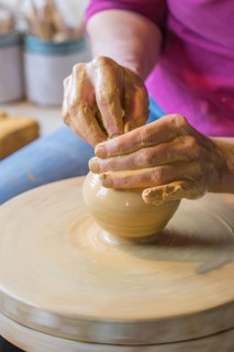 Potter turning a vase with her hands on the potter's pane