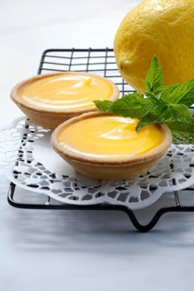 Two lemon tartlets with lemon on a cake rack
