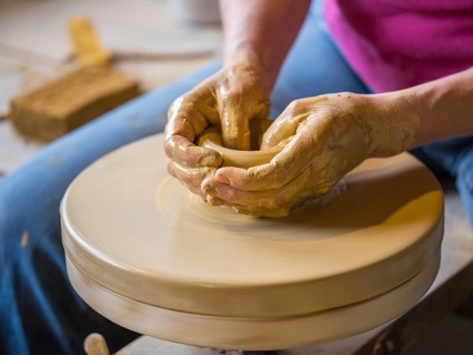 Potter turning a vase with her hands on the potter's pane