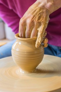 Potter turning a vase with her hands on the potter's pane