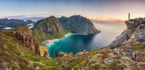 Tiny person on rocky outcrop overlooks Kvalvika beach and wide sea