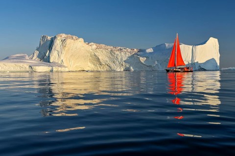 Red sailing boat in front of icebergs