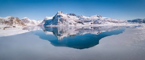 Deep wintry mountain range reflected in the blue sea