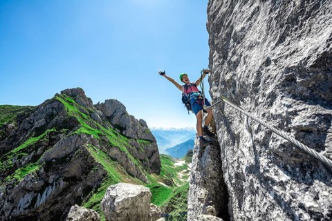 Young man stretching his arms in the air while climbing a rock face