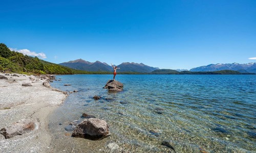 Young man stands on stone in water and stretches his arms in the air