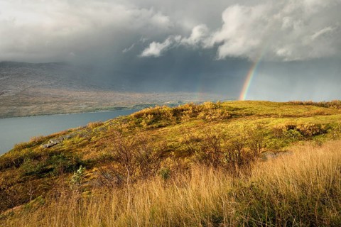 Thunderstorm with double rainbow and dramatic clouds with yellow grass on hills in autumn