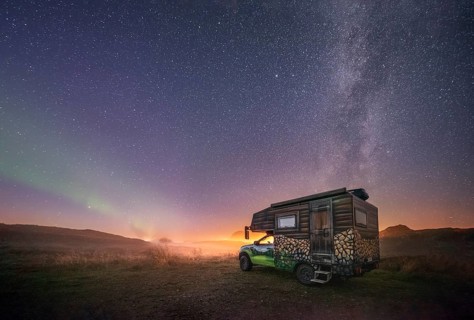 Night shot of a painted camper van under the Milky Way with northern lights