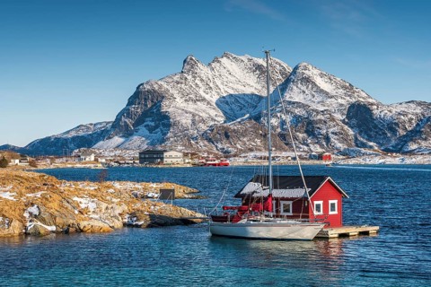 Red wooden cabin on raft with sailing boat in the sea off the coast
