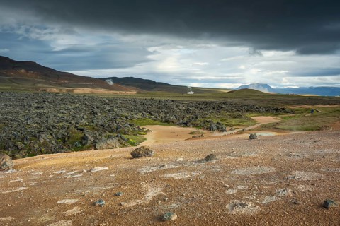 Black lava flow in Krafla lava field with geothermal power plant in the distance