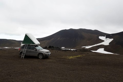Off-road vehicle with roof tent and ladder on barren plateau