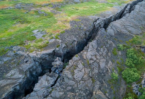 Black fissure runs through green meadow in fault zone