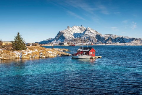 Red wooden cabin on raft with sailing boat in the sea off the coast
