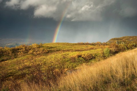 Thunderstorm with double rainbow and dramatic clouds with yellow grass on hills in autumn