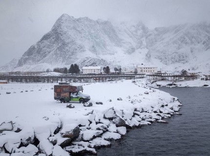 Motorhome painted as a mountain hut in snowfall at the parking lot in front of a fjord
