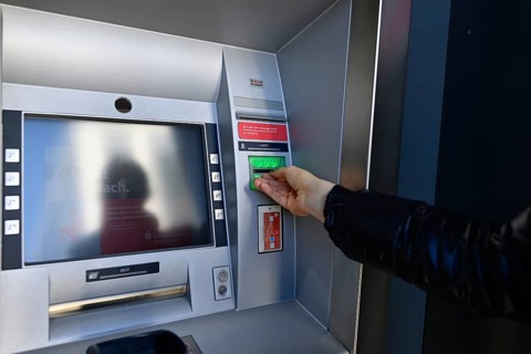 Woman waiting for the ec-card at the cash dispenser of a savings bank