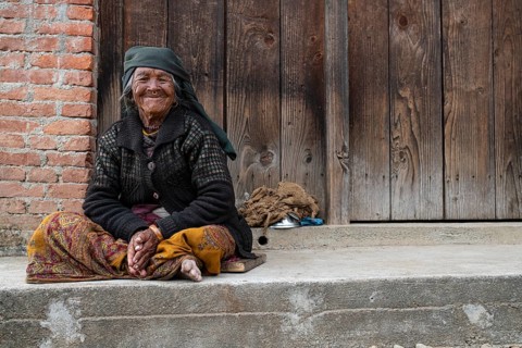 Friendly smiling elderly woman with headscarf and nose ring sitting in front of a wooden door