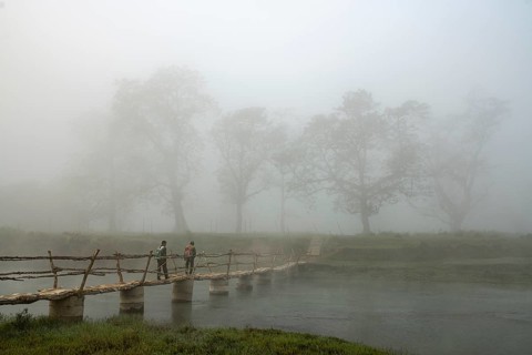 Two men walk in the morning fog over a bridge over the Rapti River