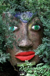 Magical woman face with red lips and green eyes looks through branches