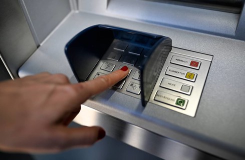 Woman typing in secret code at the cash machine of a savings bank