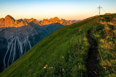 Small mountain trail with flower meadow and summit of the Uentschenspitze at sunrise