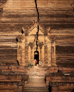 Buddhist monk stands with red umbrella in the entrance of Mingun Pagoda
