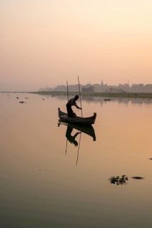 Fisherman stands with boat on the Taung Tha Man Lake to the sunrise