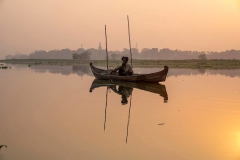 Fisherman sitting with boat on Taung Tha Man Lake at sunrise
