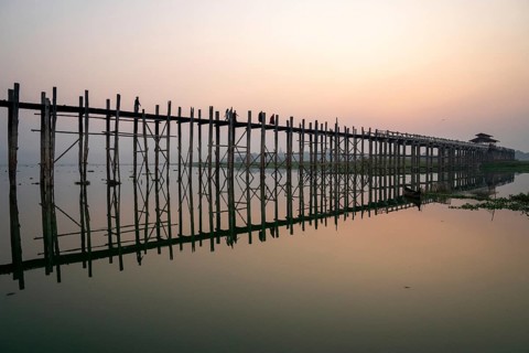 Buddhist monks walk across the U-leg bridge in red robes as the sun rises
