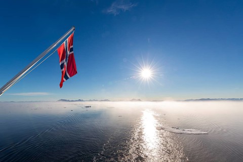 Norwegian flag waving over fjord in Greenland