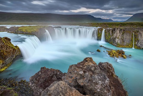 Long time exposure of a turquoise waterfall in volcanic landscape with dramatic clouds