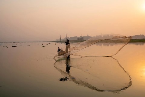 Fisherman with boat on Taung Tha Man Lake casts a fishing net for sunrise