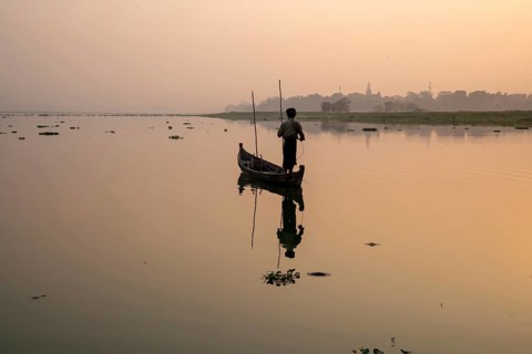 Fisherman stands with boat on the Taung Tha Man Lake to the sunrise